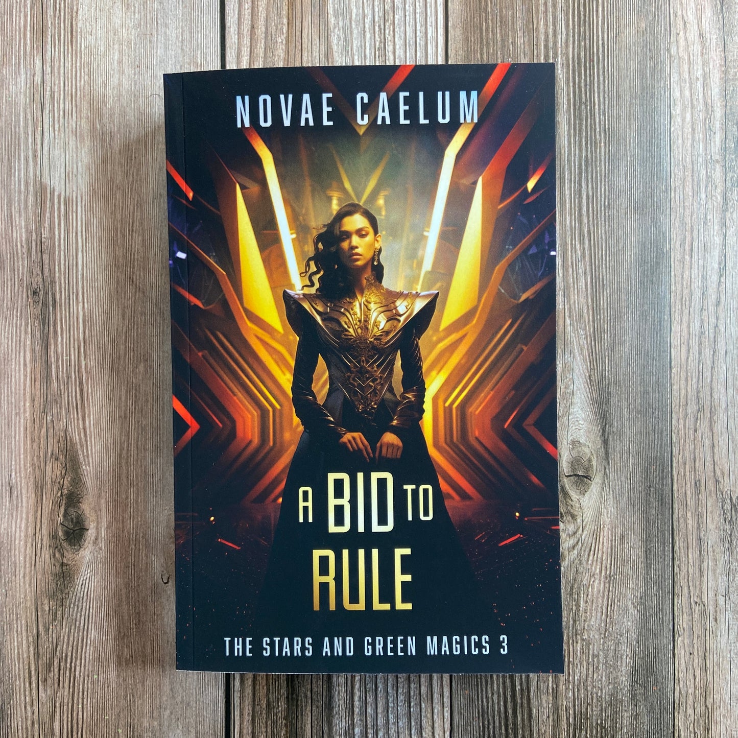 A paperback titled "A Bid to Rule: The Stars and Green Magics - Book 3" by Novae Caelum, featuring a cover image of a nonbinary individual in a futuristic gown standing with glowing waves in the background.