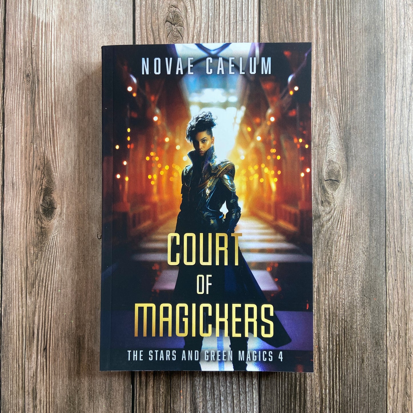 A paperback titled "Court of Magickers: The Stars and Green Magics - Book 4" by Novae Caelum, featuring a cover image of a nonbinary individual in a futuristic gown standing with glowing hallway in the background.