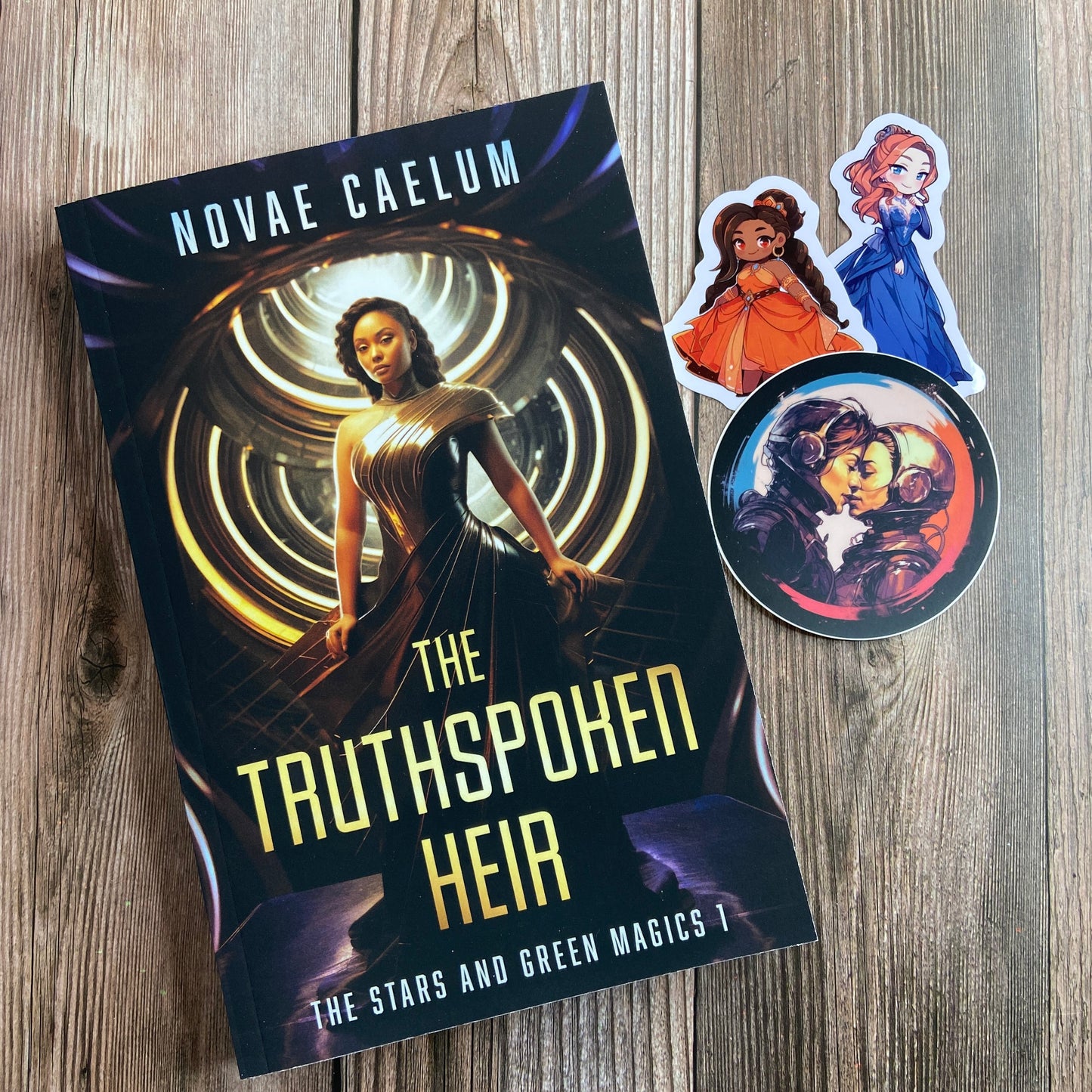 A paperback titled "The Truthspoken Heir: The Stars and Green Magics - Book 1" by Novae Caelum, featuring a cover image of a woman in a strapless, flowing gown standing with glowing rings in the background; there are also 3 series-related stickers arranged beside the book.