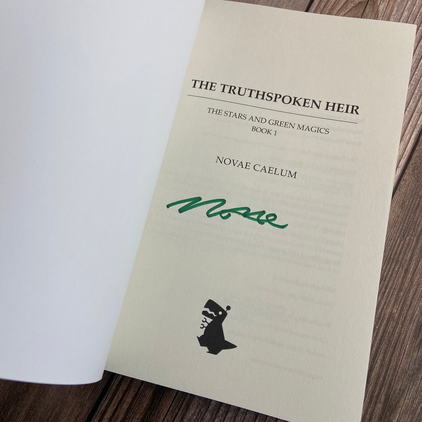 A paperback (titled "The Truthspoken Heir: The Stars and Green Magics - Book 1" by Novae Caelum) opened to display the author-signed title page.