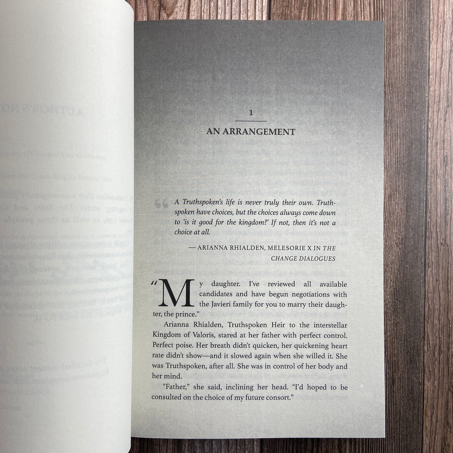 A paperback (titled "The Truthspoken Heir: The Stars and Green Magics - Book 1" by Novae Caelum) opened to display the first page of "Chapter 1: An Arrangement".