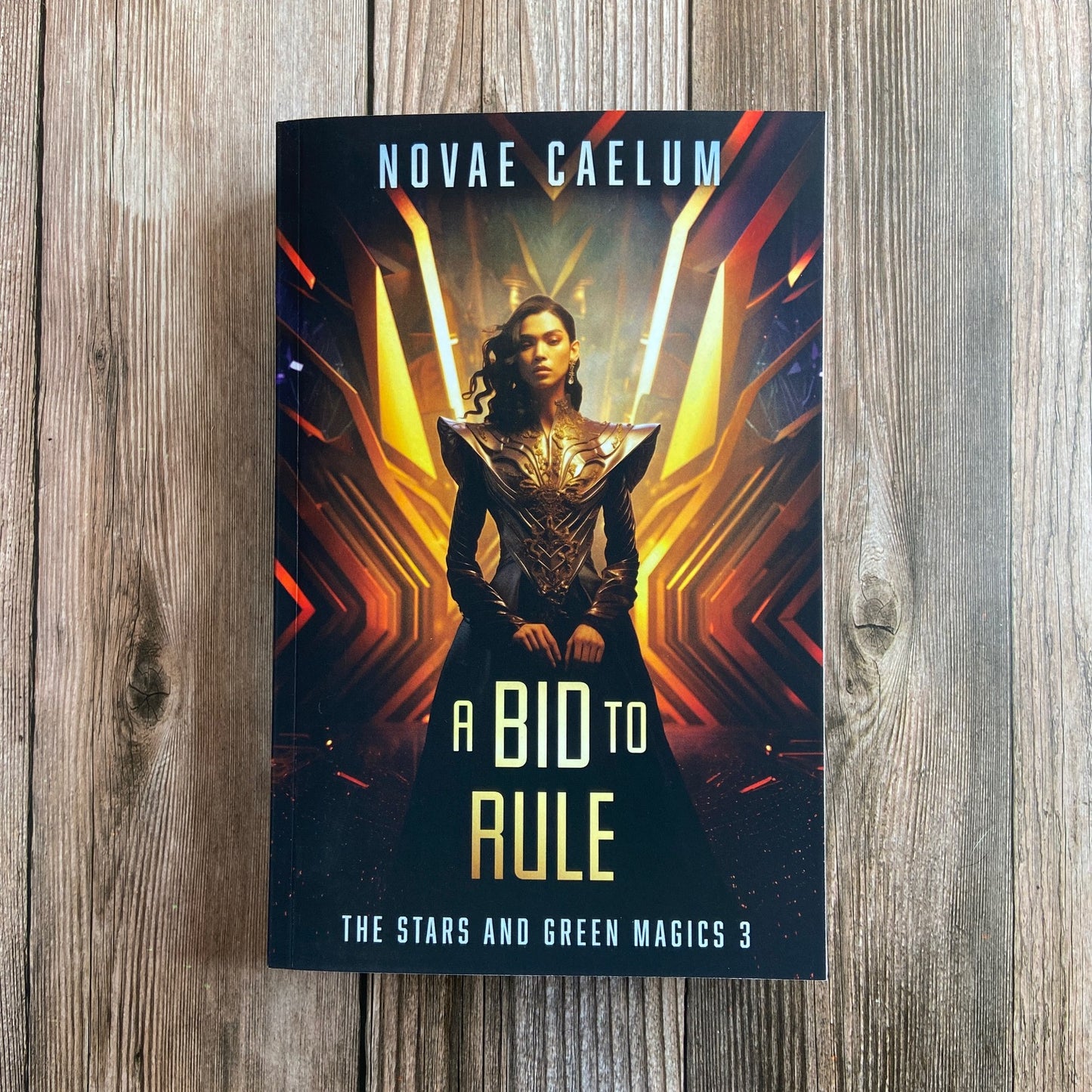 A paperback titled "A Bid to Rule: The Stars and Green Magics - Book 3" by Novae Caelum, featuring a cover image of a nonbinary individual in a futuristic gown standing with glowing waves in the background.