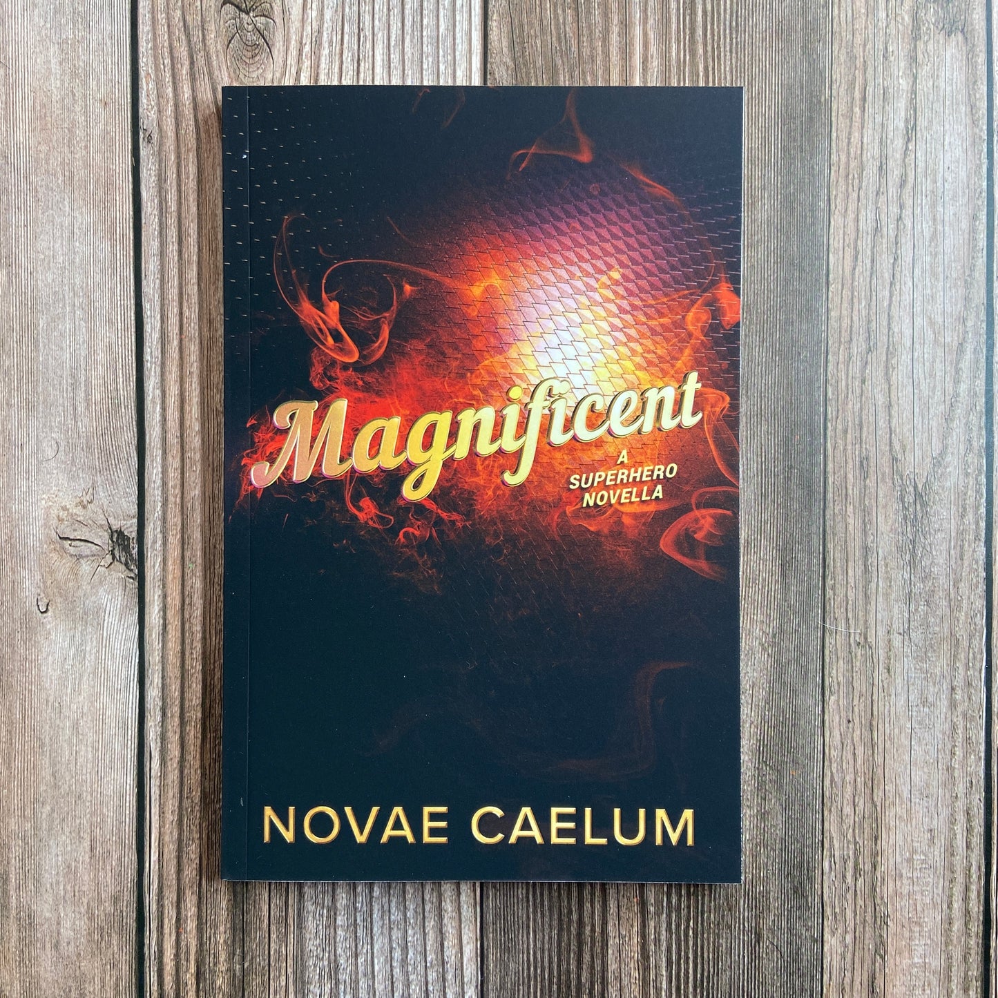 A paperback titled "Magnificient: A Nonbinary Superhero Novella" by Novae Caelum with an image of swirling red smoke on a black backdrop.