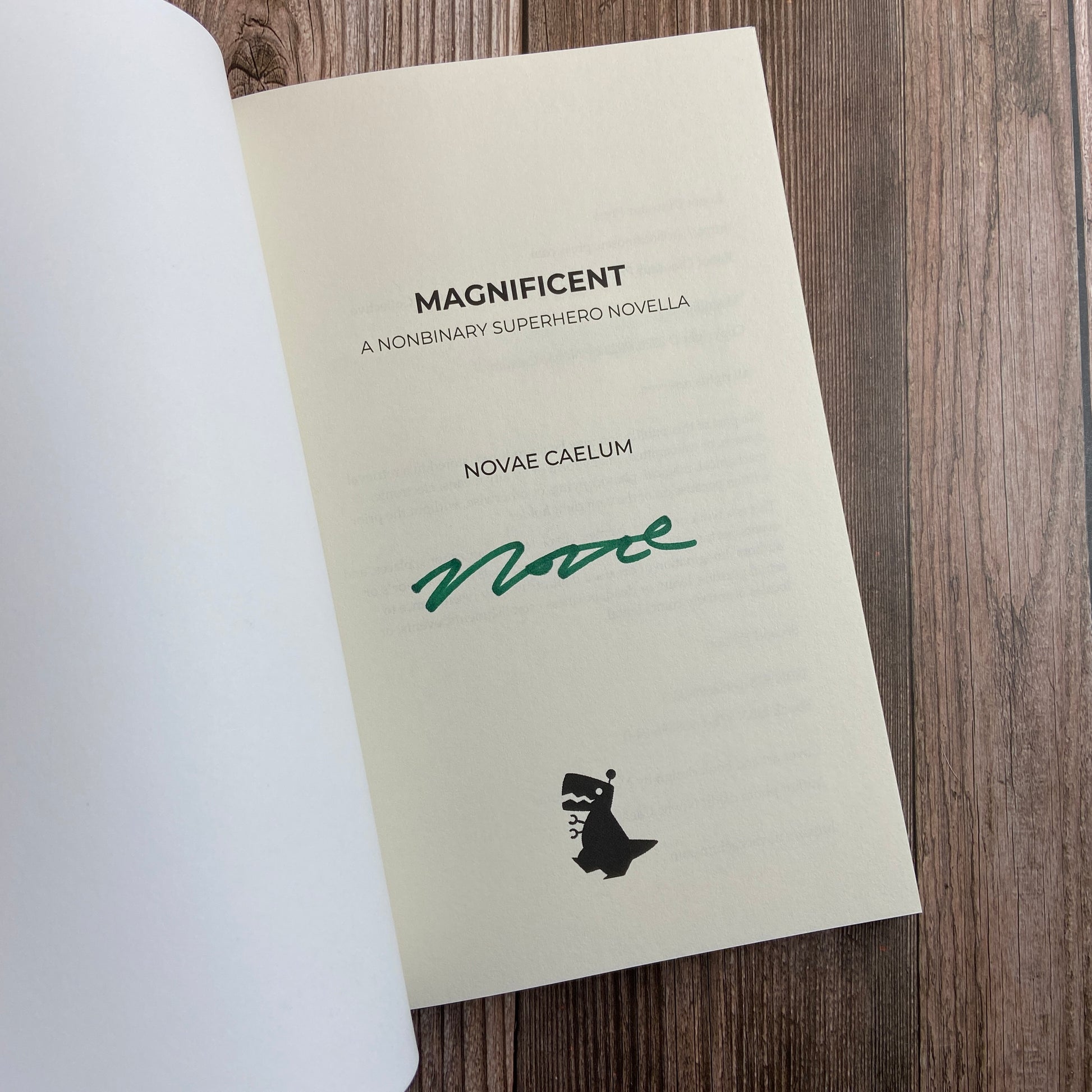 A paperback (titled "Magnificient: A Nonbinary Superhero Novella" by Novae Caelum) opened to display the author-signed title page.