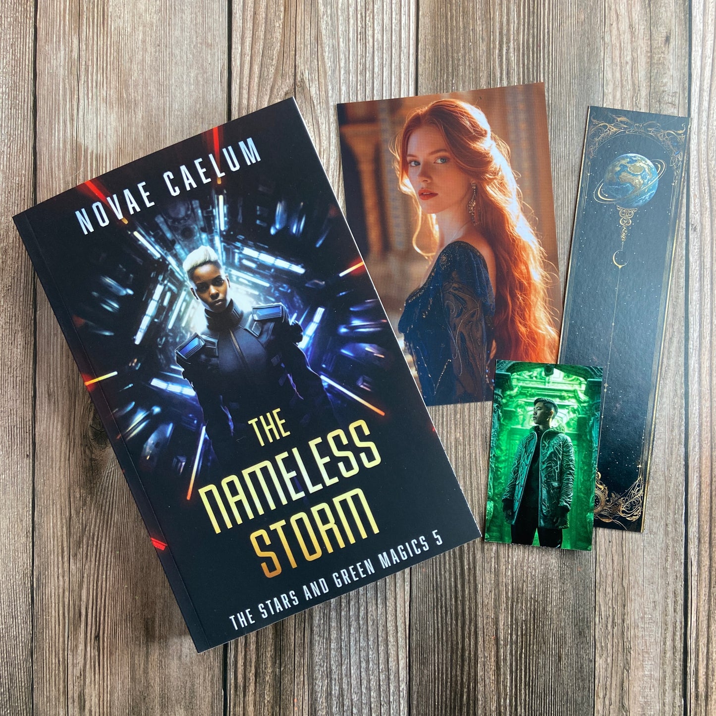 A paperback titled "The Nameless Storm: The Stars and Green Magics - Book 5" by Novae Caelum, featuring a cover image of a nonbinary individual in futuristic armor standing before a tunnel of glowing lights in the background; there are also 3 series-related swag pieces arranged beside the book.