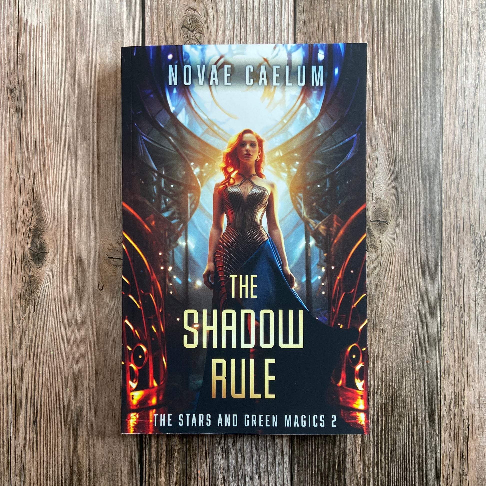 A paperback titled "The Shadow Rule: The Stars and Green Magics - Book 2" by Novae Caelum, featuring a cover image of a woman in a sleeveless, futuristic gown standing with illuminated, circular windows in the background.