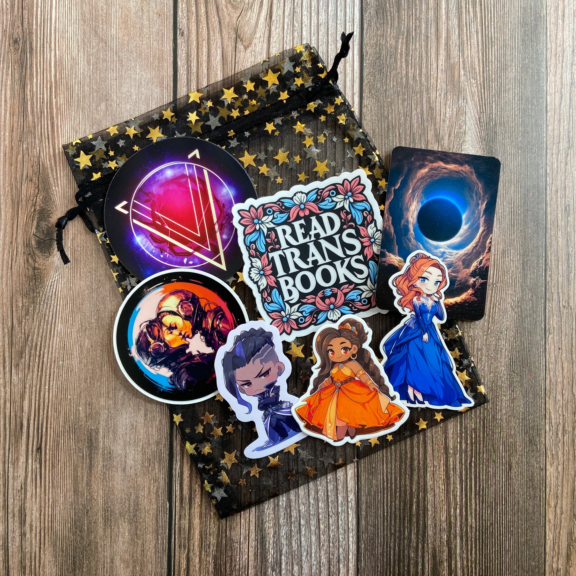 A bag with a variety of stickers on it, including ones featuring Novae Caelum's SCRATCH AND DENT - SIGNED The Stars and Green Magics Books 1-4 (Paperback) featuring trans and nonbinary main characters.