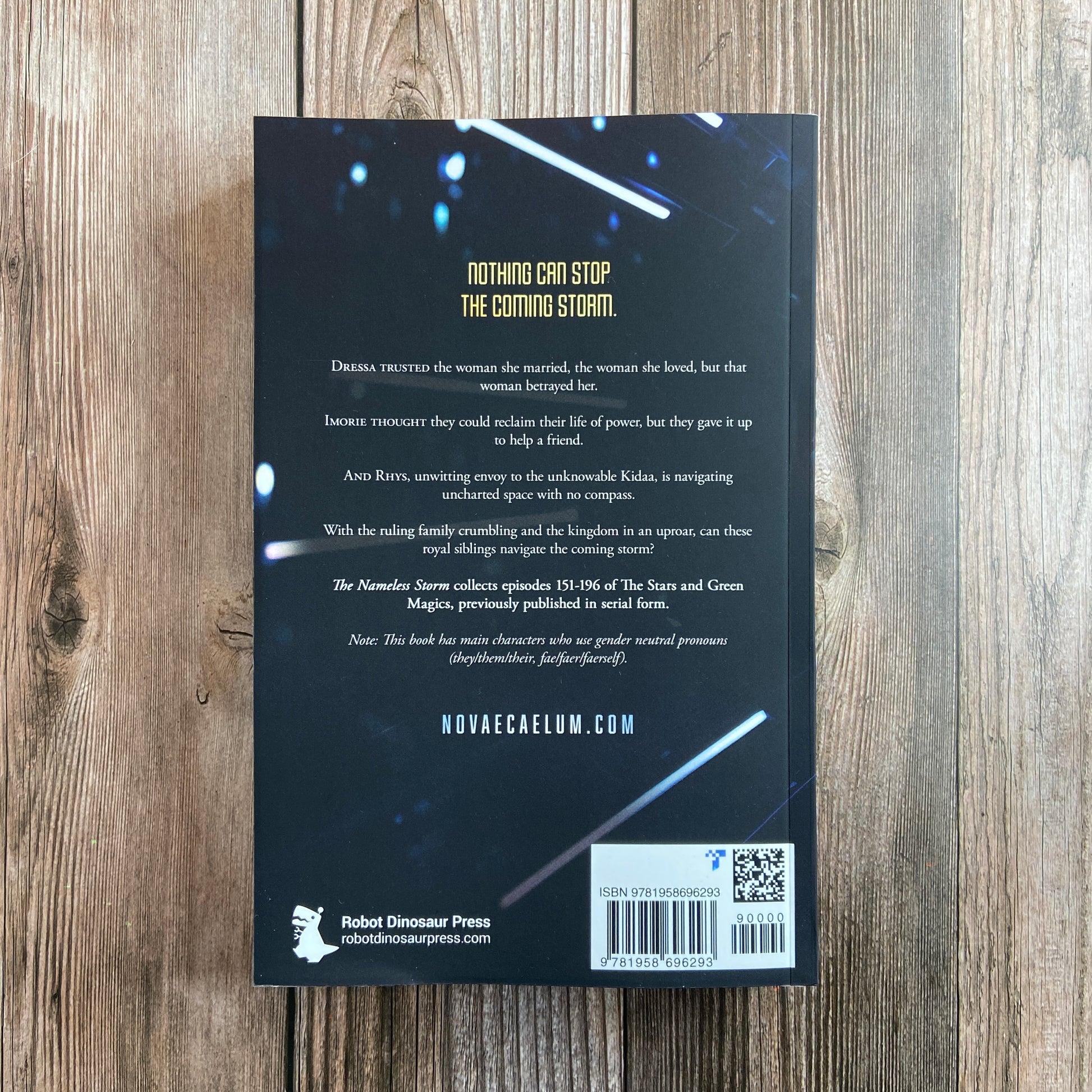 A photo of the back cover of a Novae Caelum book titled "SIGNED The Nameless Storm: The Stars and Green Magics Book 5 (Paperback)" with a description, author quotes, and website information on a wooden background.