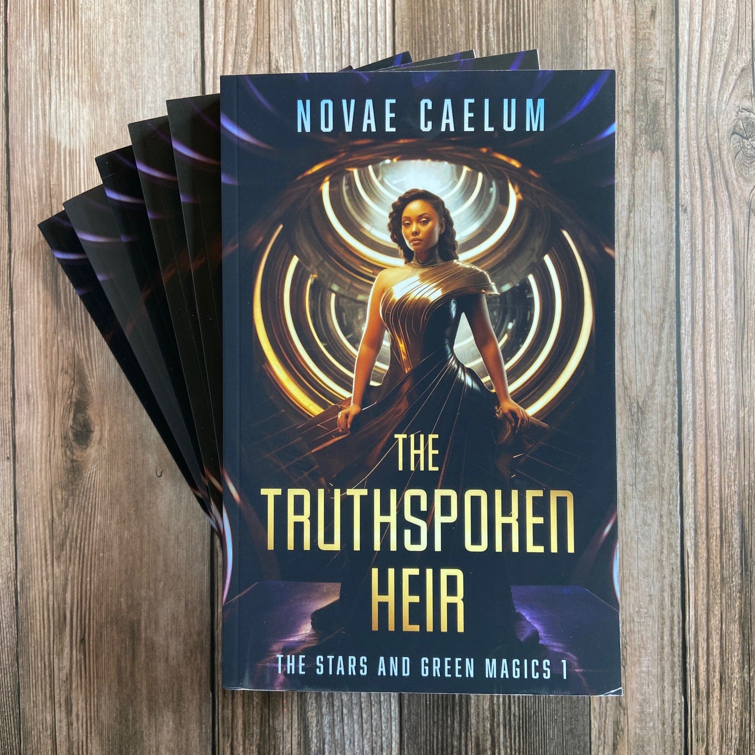 A stack of Novae Caelum books titled "SCRATCH AND DENT - SIGNED The Truthspoken Heir: The Stars and Green Magics Book 1" featuring a cover image of a woman with shapeshifting powers, standing with glowing rings in the background.