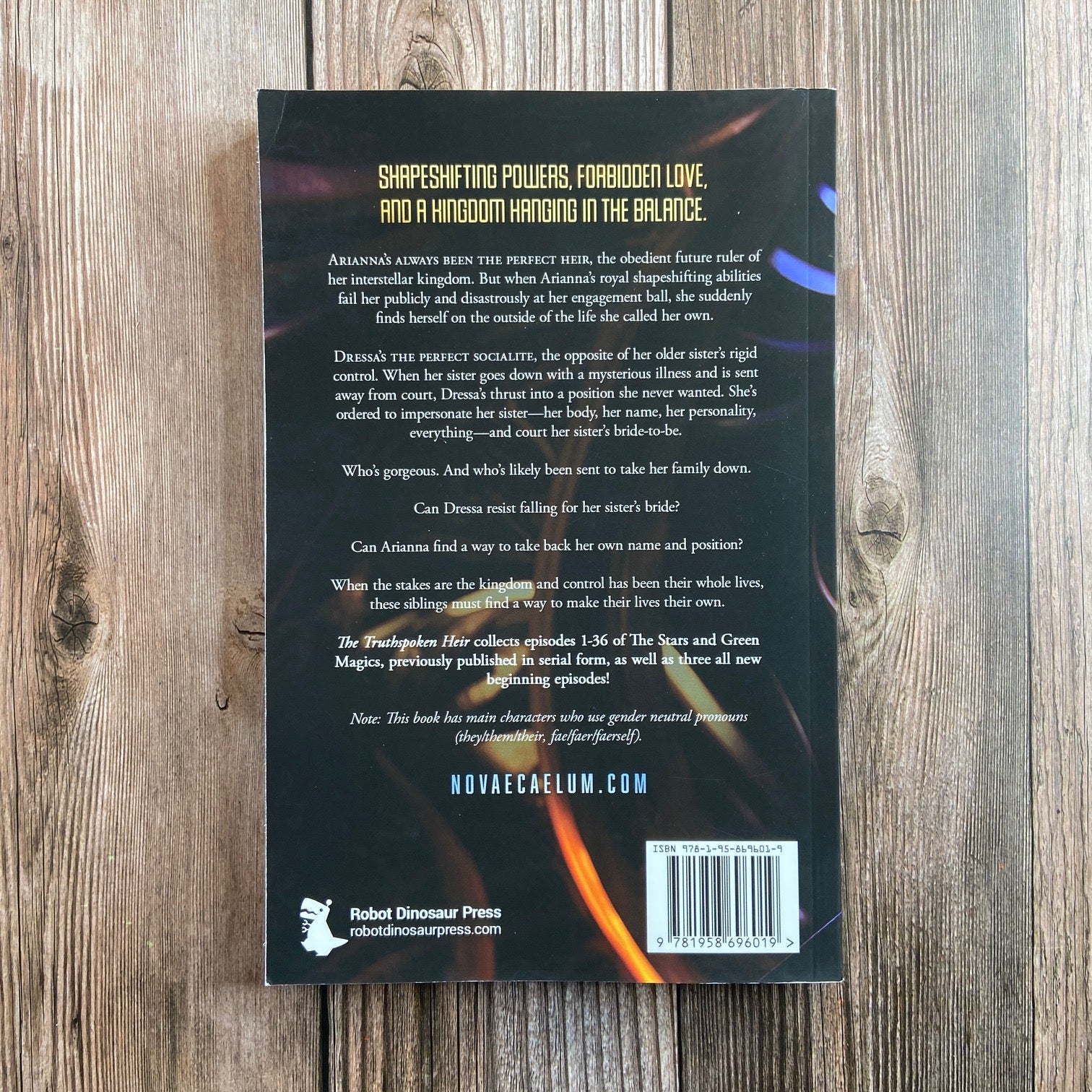 Back cover of a Novae Caelum SCRATCH AND DENT - SIGNED The Truthspoken Heir: The Stars and Green Magics Book 1 (Paperback) displayed on a wooden surface, featuring a synopsis and publisher information.